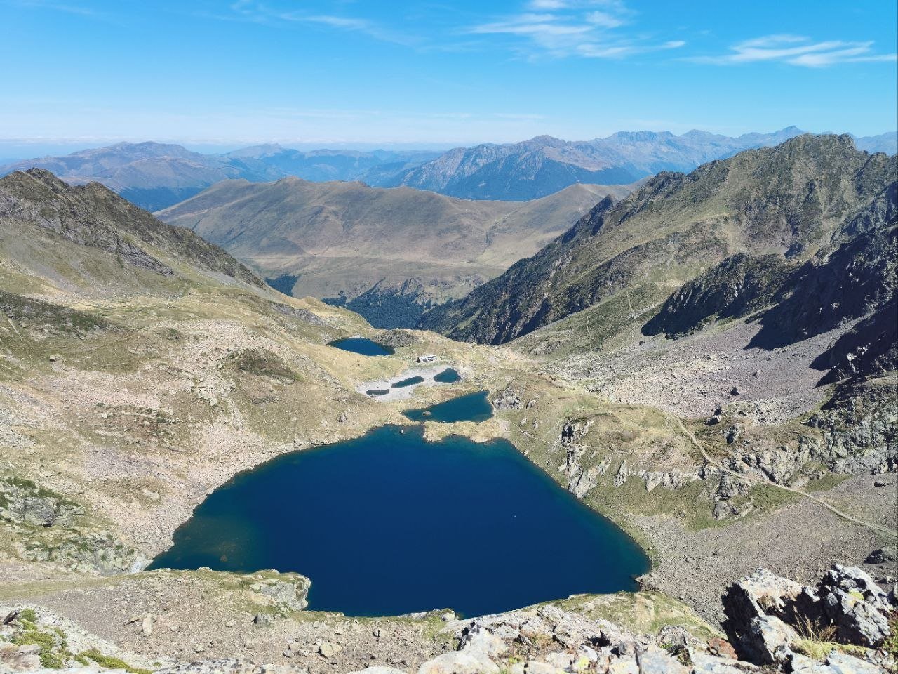 Grand lac d'altitude bleu nuit et chapelet de petits lacs autour d'un refuge, vus depuis la crête